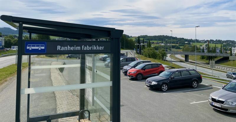 Bilde av parkeringsplass, biler og busstopp.