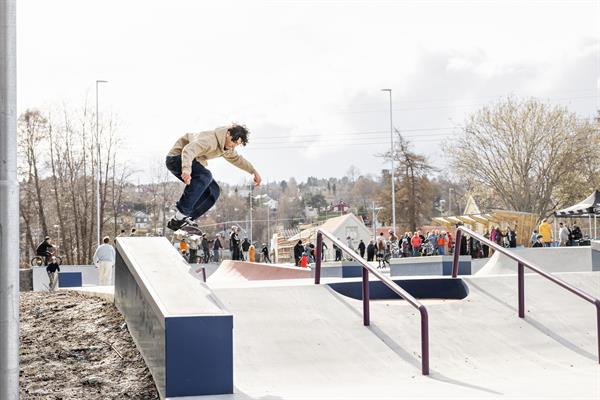 Bilde av skatepark og en person som gjør et triks med skateboard.